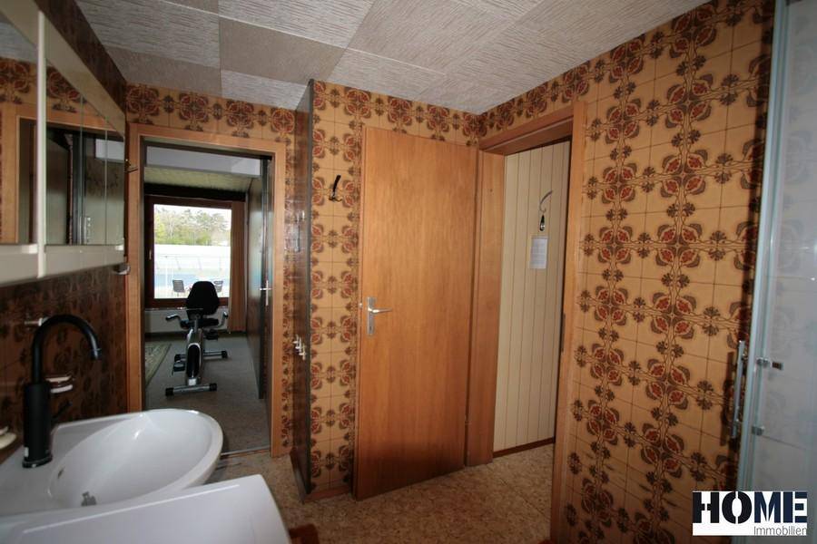 Badezimmer mit Waschbecken, gemusterter Tapete und Blick in einen angrenzenden Raum.