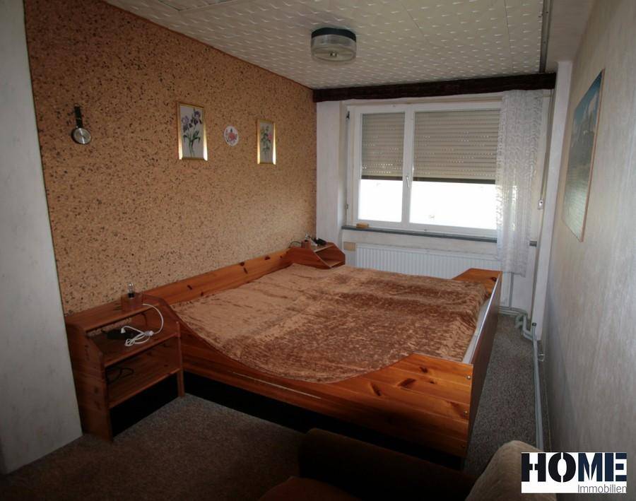 Schlafzimmer mit Holzbett, Korkwand und Fenster mit Jalousien.