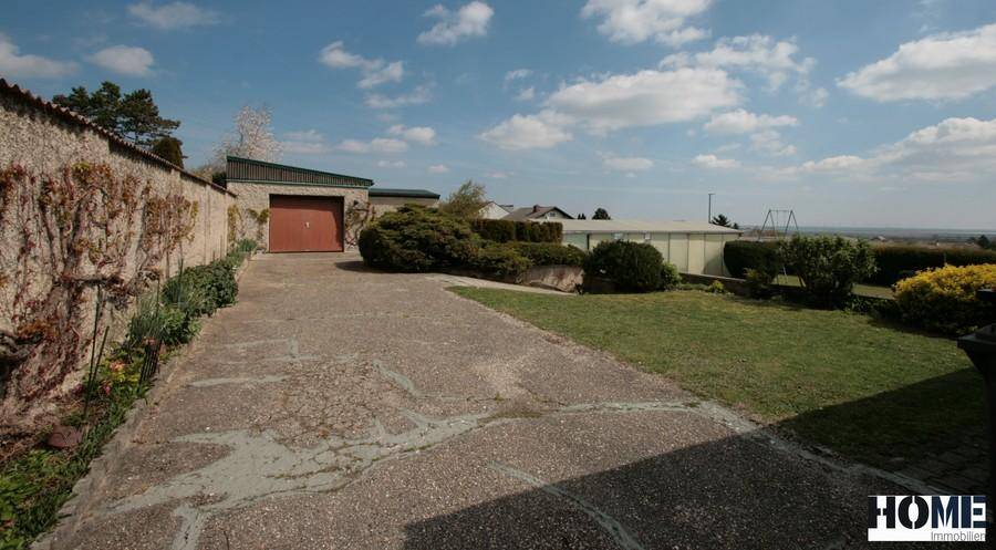 Lange Auffahrt zum Haus mit Garage, umgeben von Grünflächen und einem weiten Ausblick.