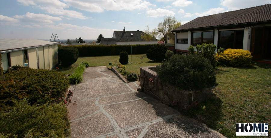 Blick auf das Haus von der Seite mit Garten, gepflastertem Weg und weitem Blick in die Landschaft.