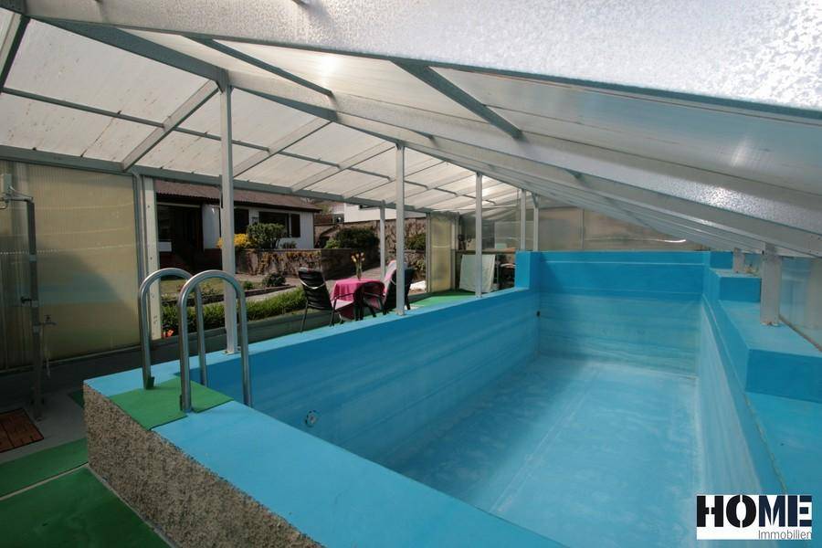 Überdachter Poolbereich mit blauem Becken und Blick auf den Garten.