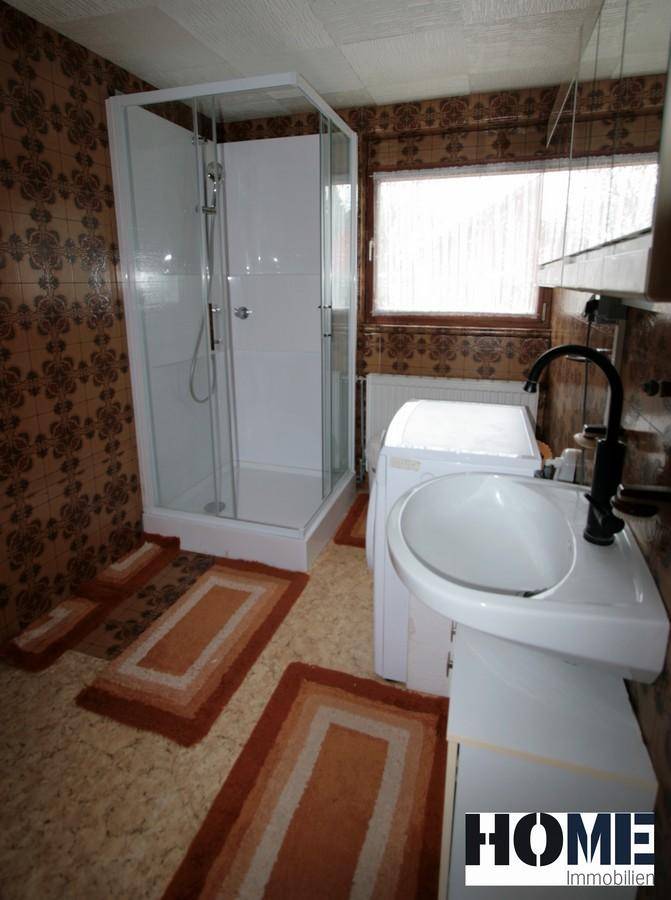 Badezimmer mit Duschkabine, Waschbecken und gemusterten Fliesen im 80er-Jahre-Stil.