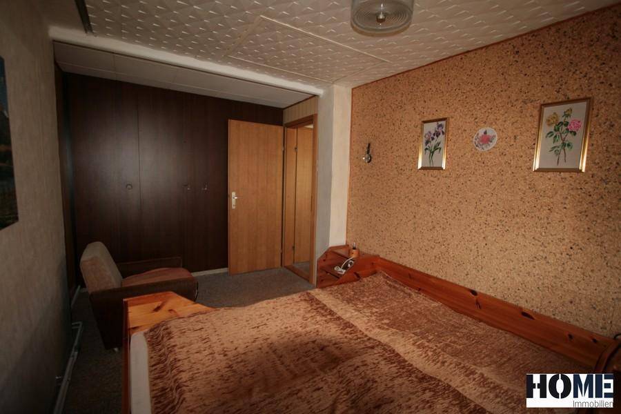 Schlafzimmer mit Holzbett, Einbauschränken und Zugang zu weiteren Räumen.