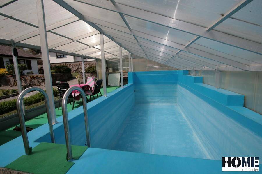 Innenansicht des überdachten Schwimmbades mit blauem Becken und transparenter Dachkonstruktion.