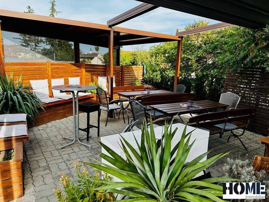 Gemütlicher Außenbereich mit überdachter Terrasse, Holzbänken und Tischen, umgeben von Pflanzen.