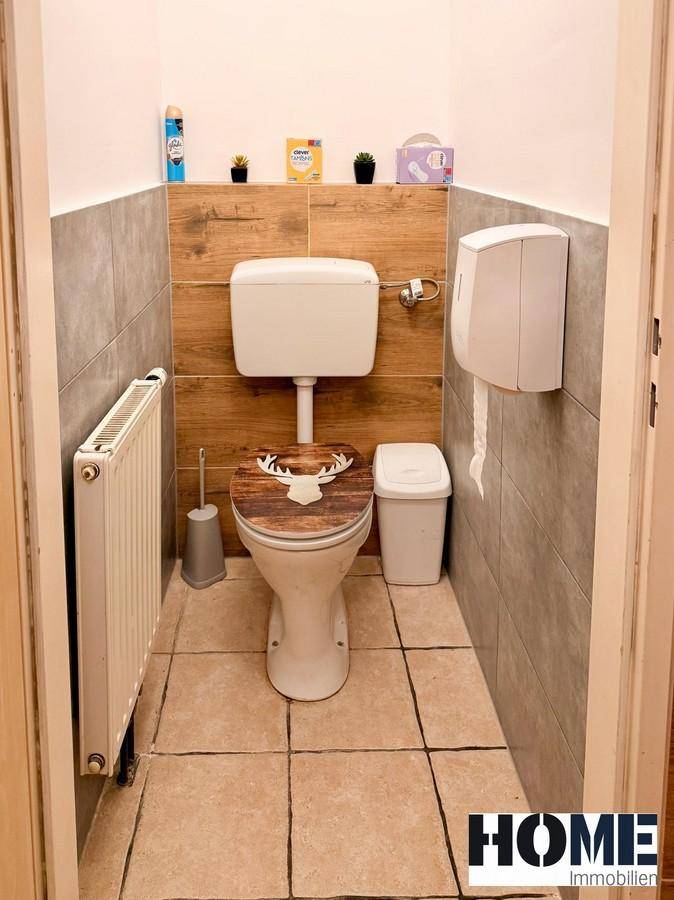 Sauberer Toilettenraum mit WC, Heizkörper und Spender, dekoriert mit Holzpaneelen und Fliesen.