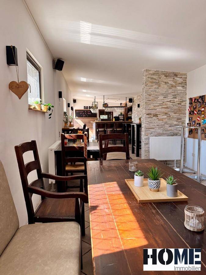 Geräumiger Gastraum mit verschiedenen Sitzbereichen, Holztischen und einer Bar im Hintergrund.
