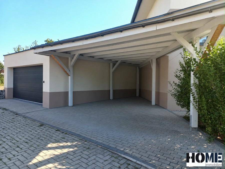 Geräumiger Carport und eine moderne Garage mit dunklem Rolltor neben dem Haus.