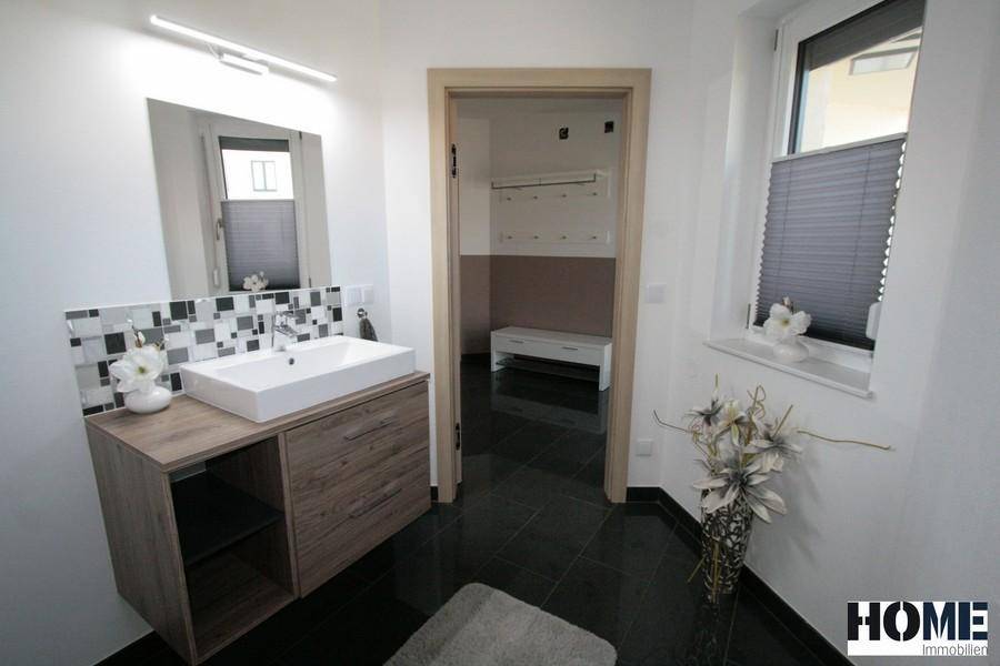 Helles Badezimmer mit modernem Waschbecken, Spiegel und Zugang zum Flur.