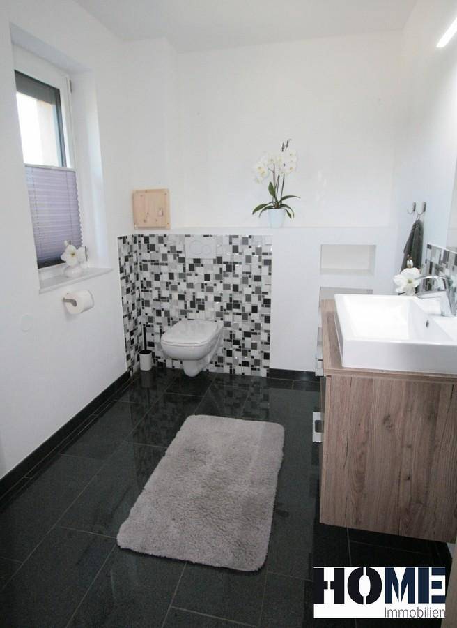 Modernes Badezimmer mit dunklen Fliesen, Wand-WC und einem Waschbeckenunterschrank aus Holz.