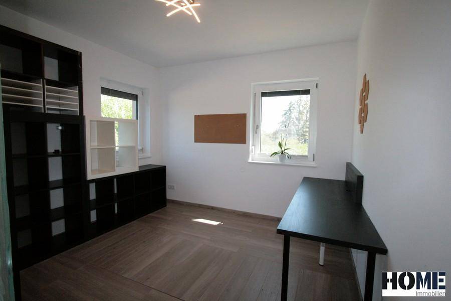 Helles Arbeitszimmer mit Holzboden, zwei Fenstern und praktischen Regalen.