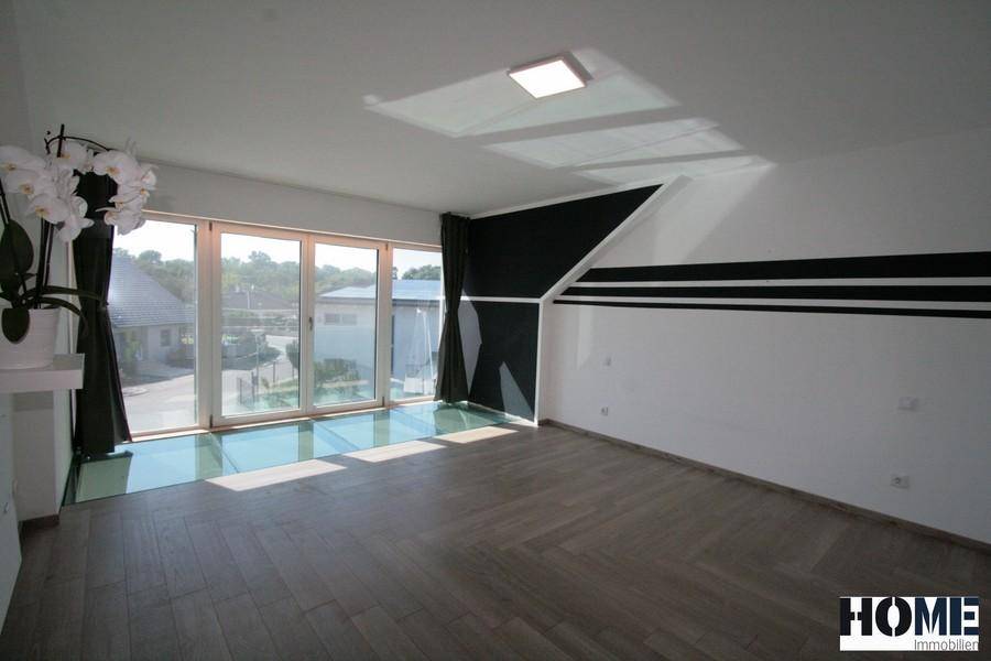 Heller Wohnraum mit großen Glasfronten, Glasboden und Holzboden, der viel Tageslicht hereinlässt.