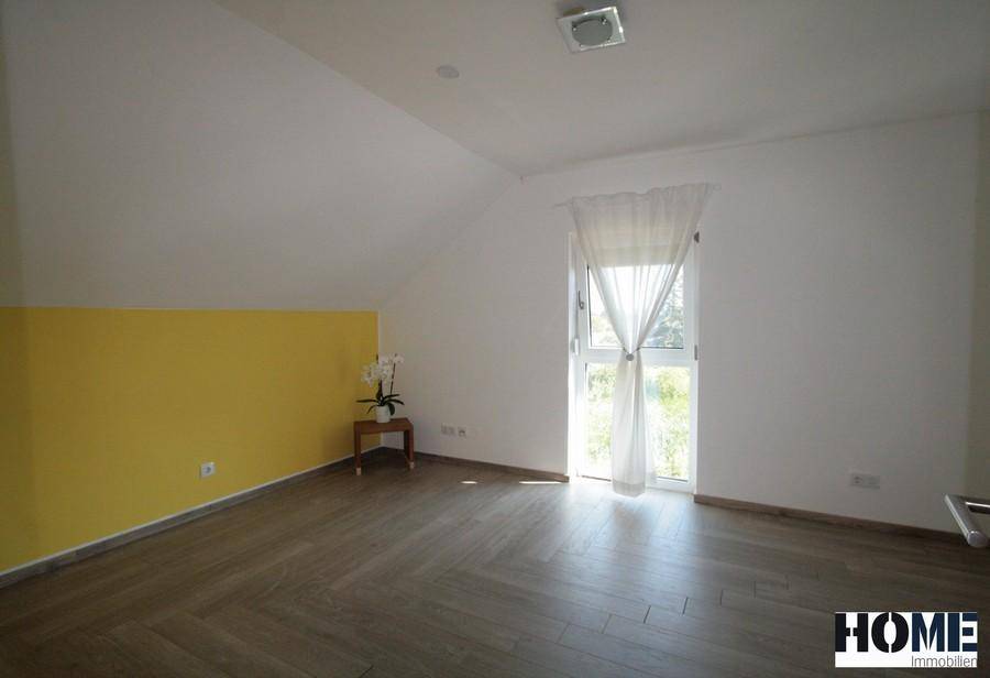 Helles Zimmer mit gelber Akzentwand, Holzboden und Dachschräge.