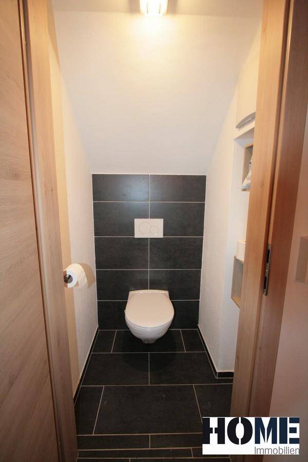 Praktisches Gäste-WC im Untergeschoss mit dunklen Fliesen und Wand-WC.