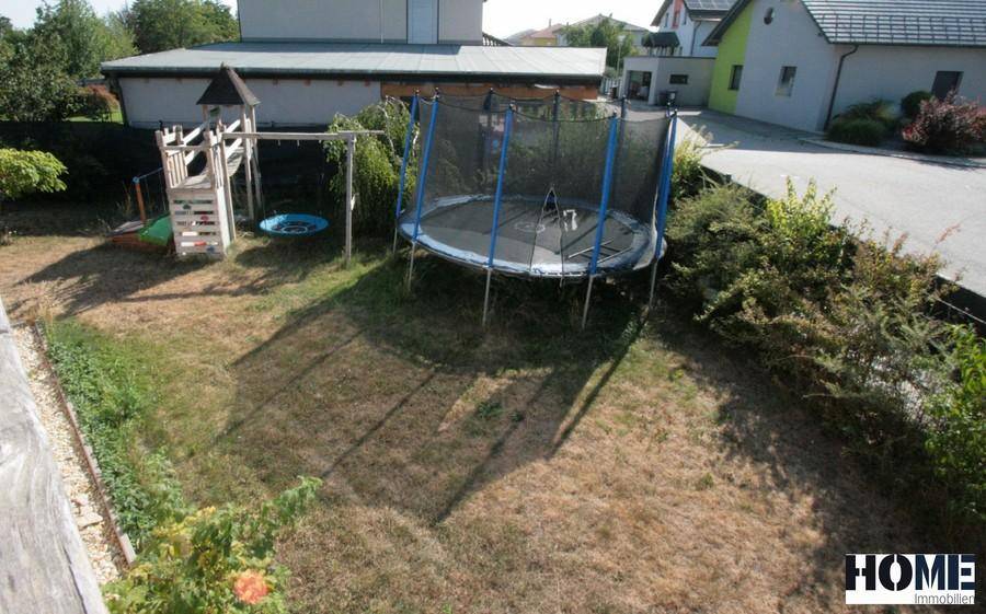 Garten mit Rasenfläche, einem Trampolin und einem Spielplatz für Kinder.