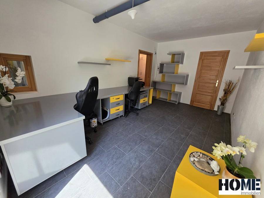 Geräumiges Büro mit mehreren Arbeitsplätzen, dunklen Fliesen und modernen Regalsystemen.