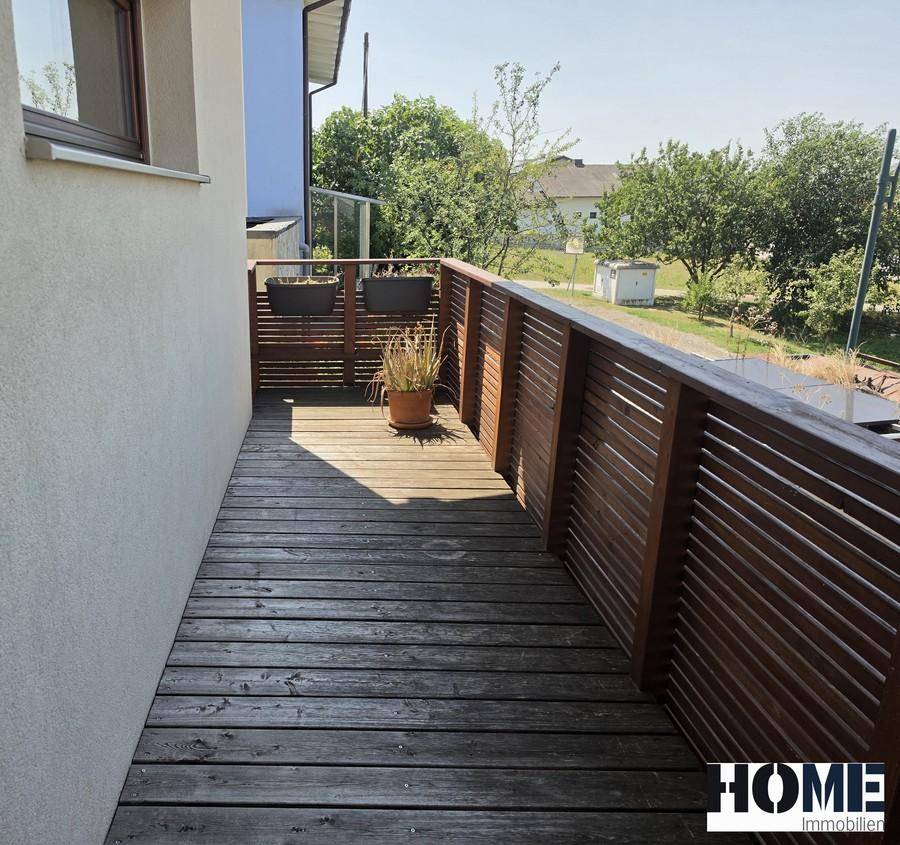 Sonniger Balkon mit Holzboden und Holzgeländer, bietet einen weiten Blick ins Grüne.