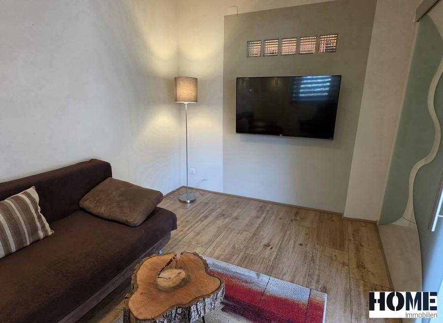 Wohnzimmer mit Wandfernseher, Sofa und Stehlampe, bietet eine entspannte Atmosphäre.