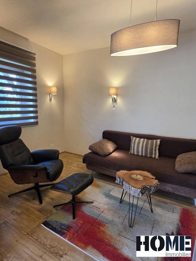 Gemütliches Wohnzimmer mit Sofa, Sessel, Holzboden und modernem Couchtisch aus Holz.