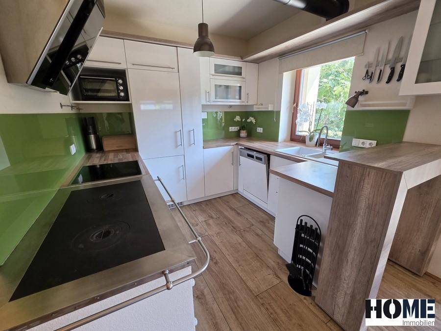 Moderne Küche mit weißen Schränken, Holz-Arbeitsplatten, grünem Fliesenspiegel und Induktionskochfeld.