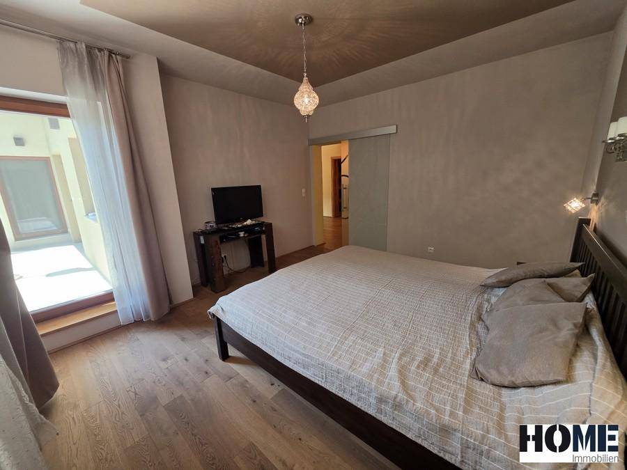 Schlafzimmer mit Holzboden, Zugang zu einem kleinen Balkon und einer modernen Schiebetür.