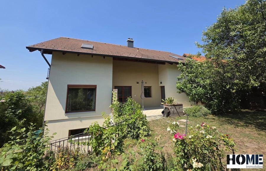 Rückansicht des Hauses mit kleiner Terrasse und einem grünen, leicht abfallenden Gartenbereich.