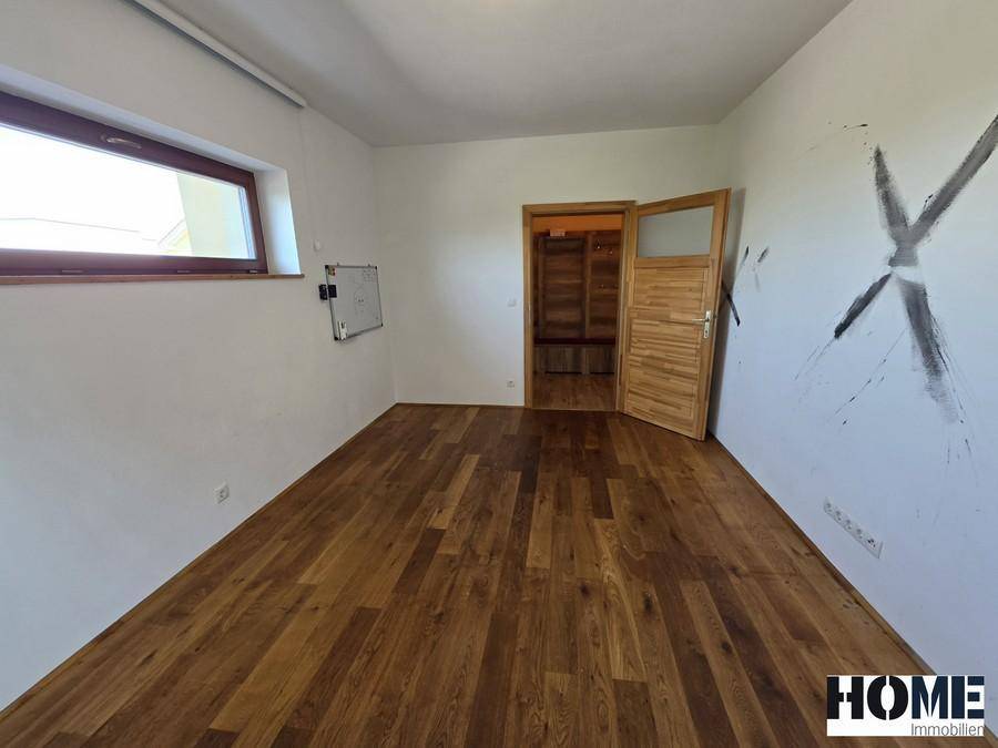 Geräumiger leerer Raum mit Holzdielenboden und einer Holztür, die zu einem weiteren Bereich führt.