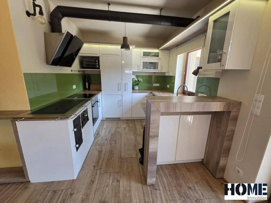 Moderne Küche mit weißen Schränken, grüner Rückwand und Holzbodenoptik, inklusive Frühstücksbar.