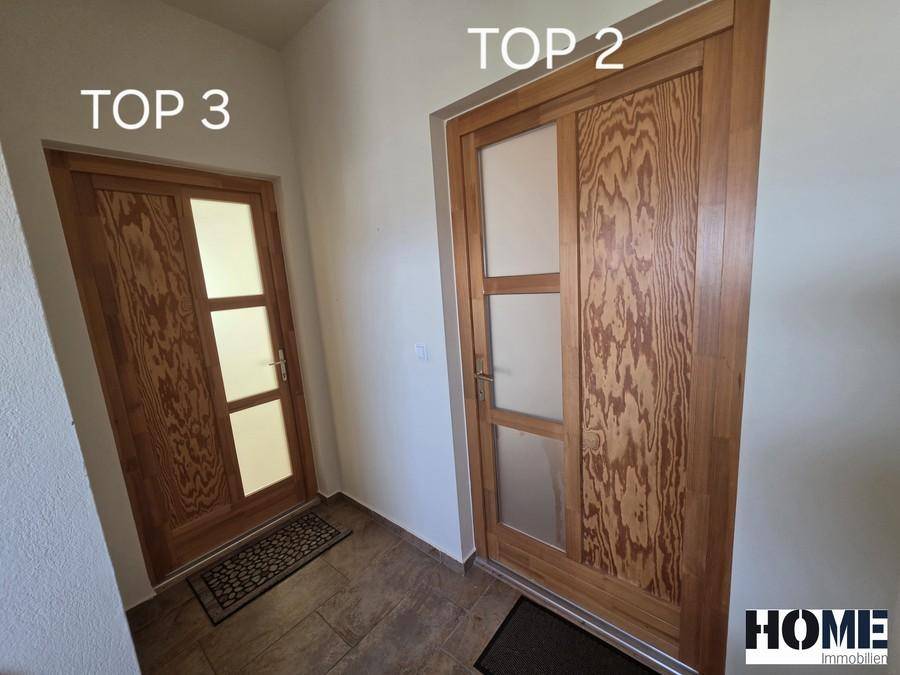 Zwei Wohnungseingangstüren, beschriftet mit "TOP 3" und "TOP 2", in einem hellen Flurbereich.