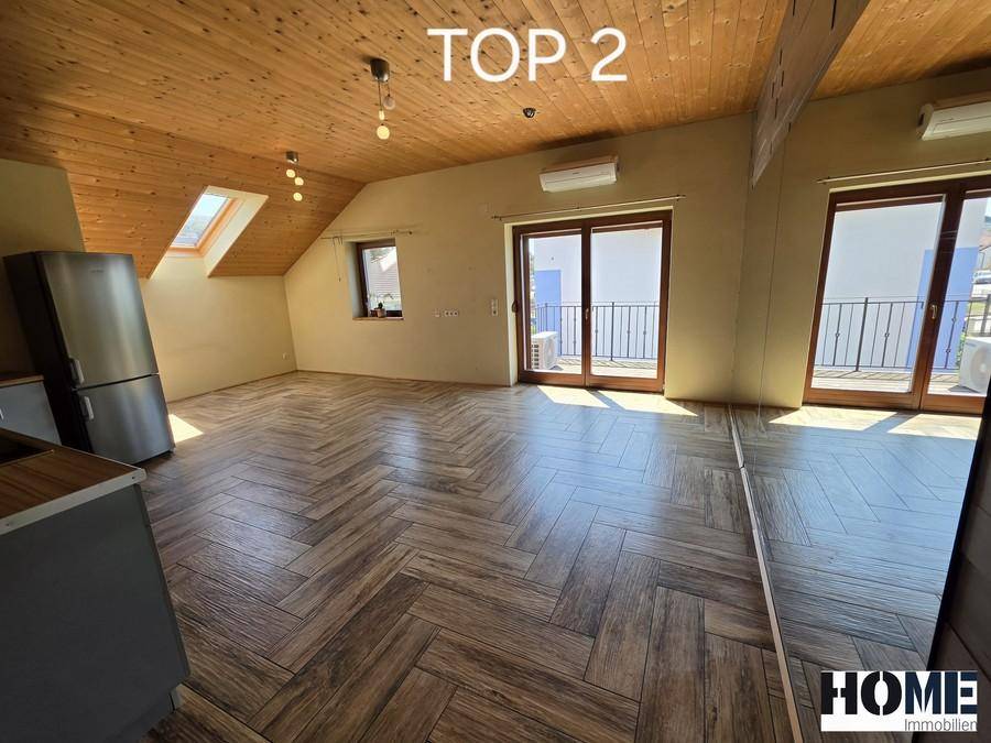 Heller Wohnbereich mit Holzdecken, Holzbodenoptik und Zugang zu einem französischen Balkon.
