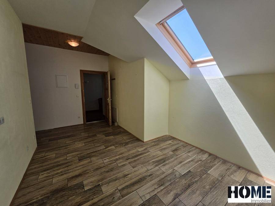 Helles Zimmer im Dachgeschoss mit Holzbalkendecke, Dachfenster und Fliesenboden in Holzoptik.