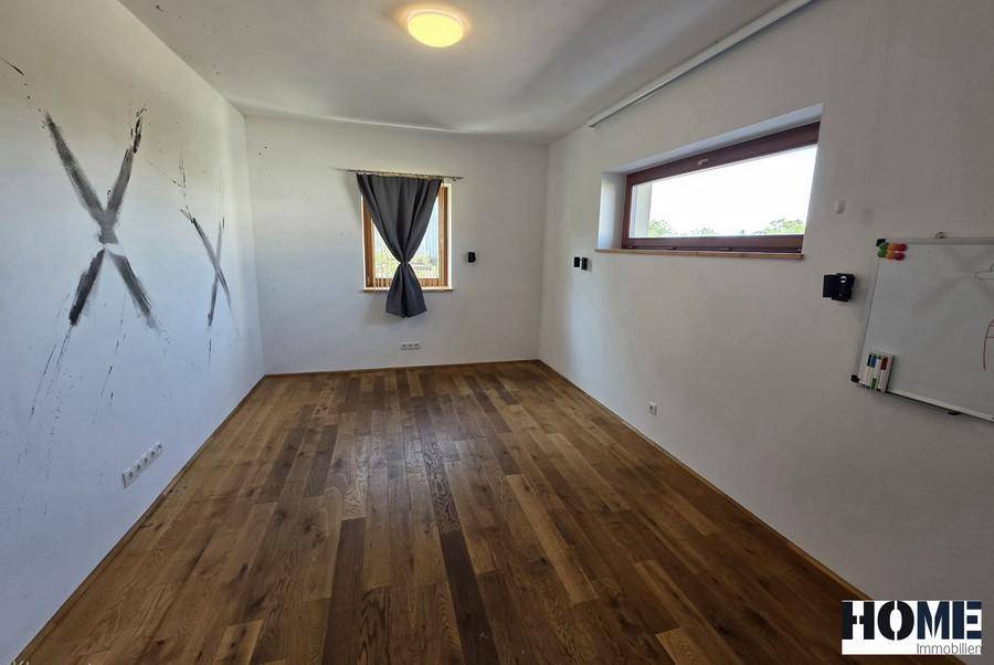 Leerer Raum mit Holzdielenboden und zwei Fenstern, die für ausreichend Tageslicht sorgen.