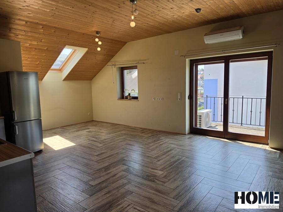 Geräumiger Wohnbereich mit schräger Holzdecke, Dachfenster und Zugang zu einem französischen Balkon.