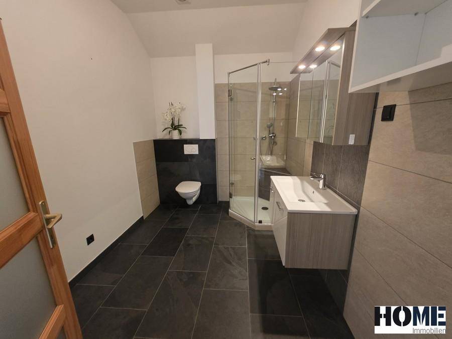Modernes Badezimmer mit dunklen Fliesen, wandhängendem WC, Duschkabine und Waschtisch.