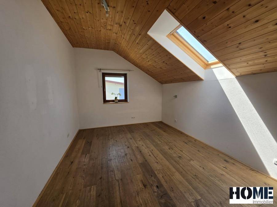 Heller Raum mit schräger Holzdecke, Holzdielenboden und einem Dachfenster für viel Licht.