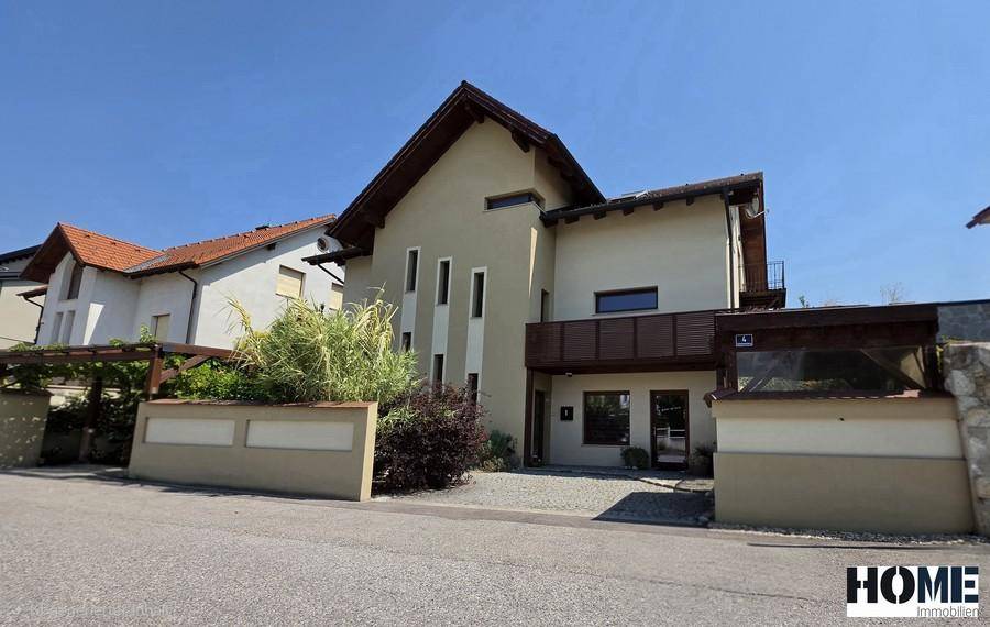 Moderne Hausfassade mit ansprechendem Design, großen Fenstern und einem kleinen Balkon.