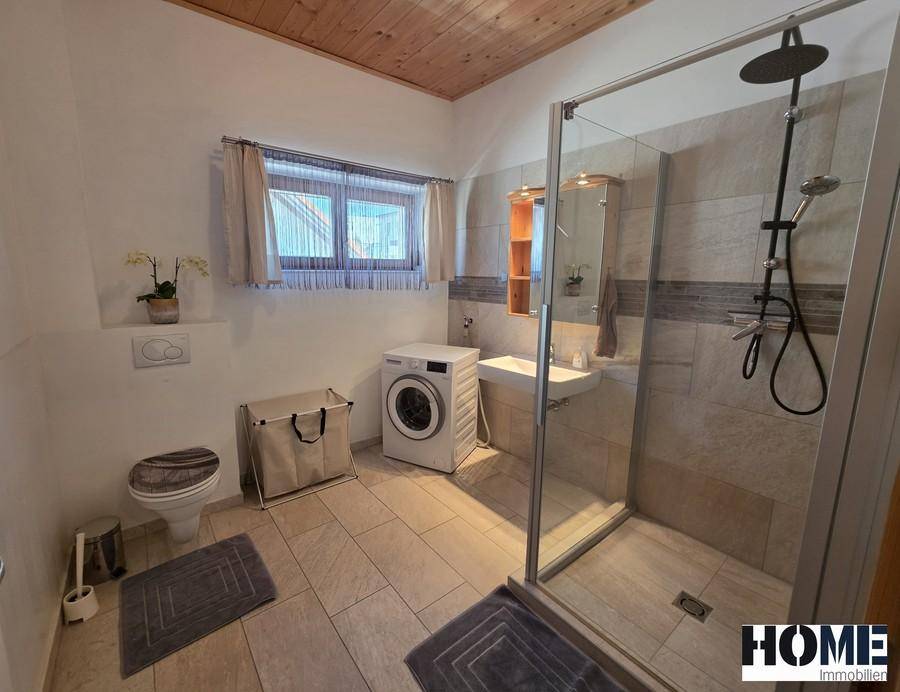 Modernes Badezimmer mit ebenerdiger Dusche, Waschmaschine und Fenster für Tageslicht.