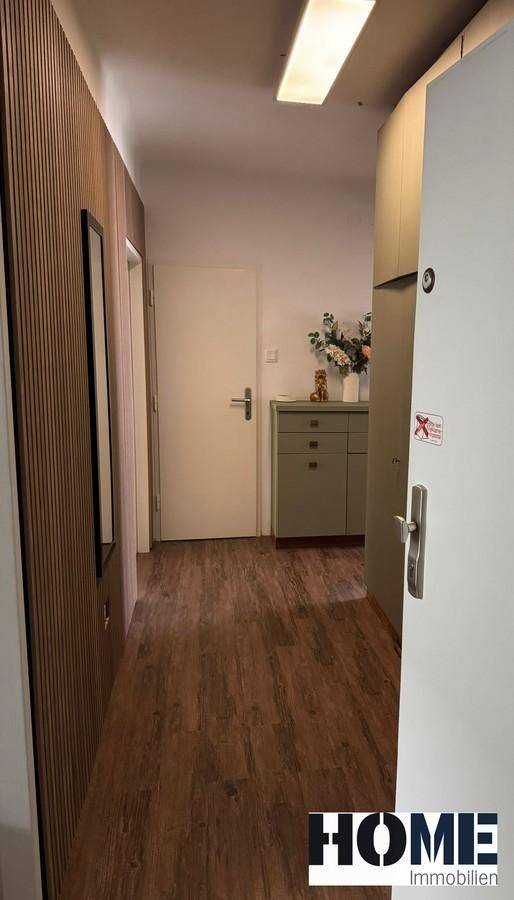 Heller Flur mit Holzpaneelen, Garderobenschrank und Holzboden, der zu weiteren Räumen führt.