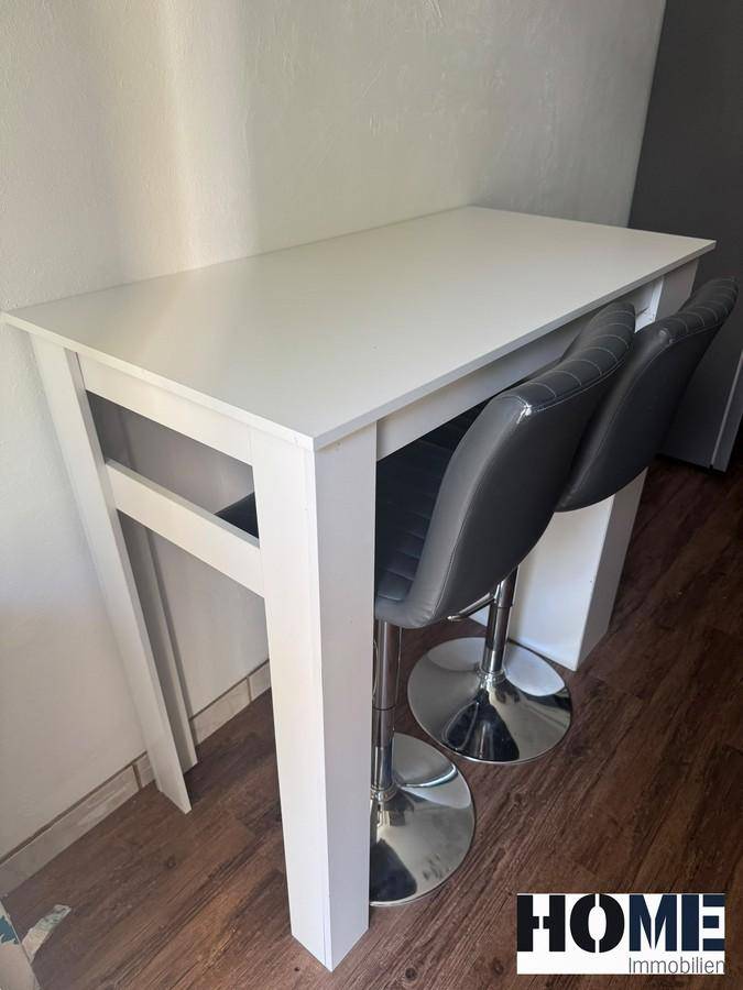 Weißer Bartisch mit zwei modernen Barhockern, ideal für schnelle Mahlzeiten oder als Arbeitsfläche.