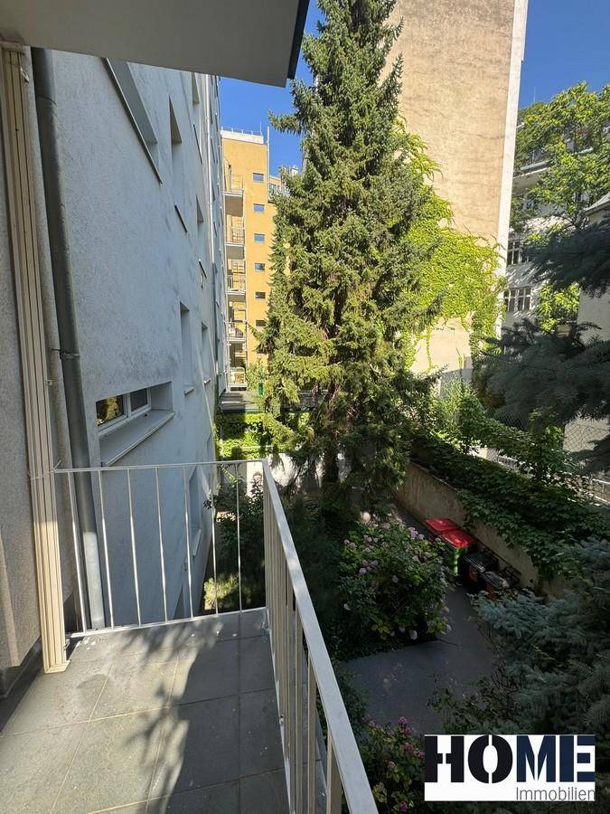Balkon mit Fliesenboden und Blick auf einen begrünten Innenhof und umliegende Gebäude.