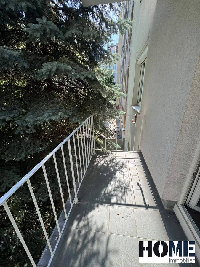 Schmaler Balkon mit weißem Geländer und Fliesenboden, bietet einen Blick auf hohe Bäume.