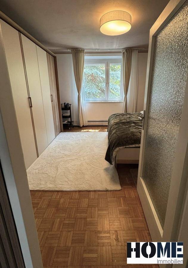 Schlafzimmer mit Parkettboden, großem Kleiderschrank und Fenster mit Blick ins Grüne.