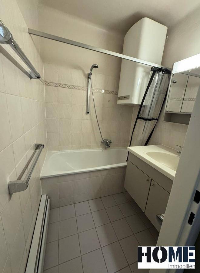 Badezimmer mit Badewanne, integrierter Dusche, Waschbecken und hellen Fliesen an Wänden und Boden.