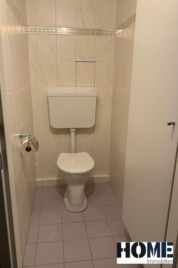 Separates WC mit Toilette und hellen Fliesen an Wänden und Boden, in einem kompakten Raum.