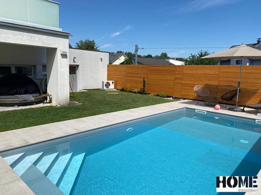 Moderner Poolbereich mit Treppeneinstieg, umgeben von Rasen und der Hausfassade.