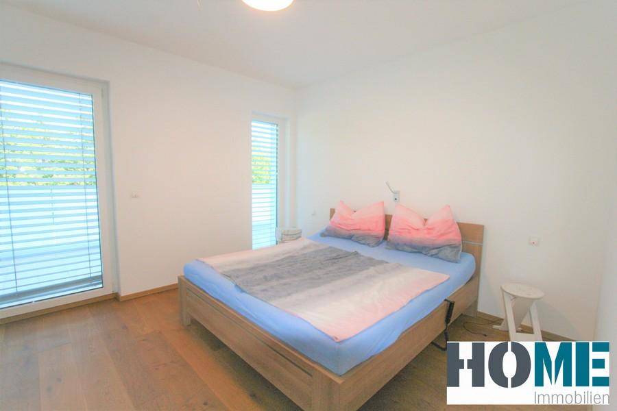 Helles Schlafzimmer mit Holzboden und großem Fenster, das viel Tageslicht hereinlässt.
