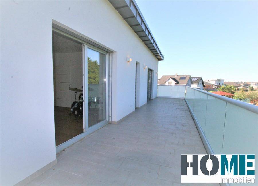 Langer Balkon mit Fliesenboden und Glasgeländer, bietet Zugang zu mehreren Räumen und Weitblick.