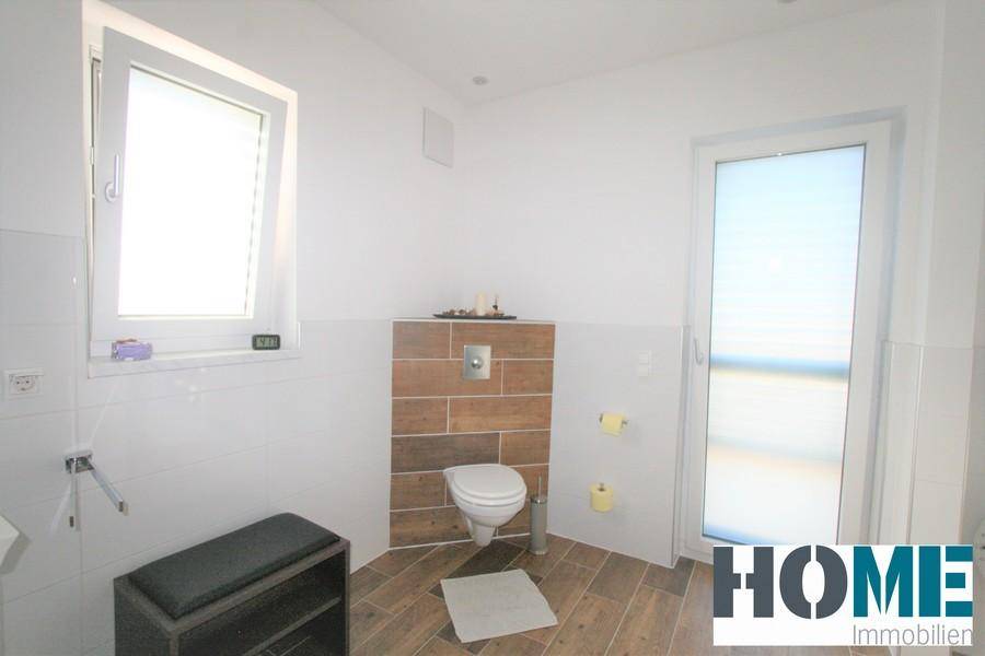Badezimmer mit wandhängendem WC, Fenster und Zugang zum Balkon, hell und modern gestaltet.