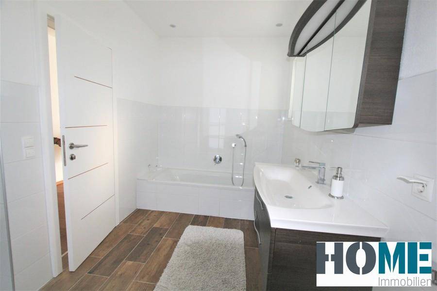 Modernes Badezimmer mit Badewanne, Einzelwaschbecken und Spiegelschrank, ausgestattet mit Holzoptikfliesen.