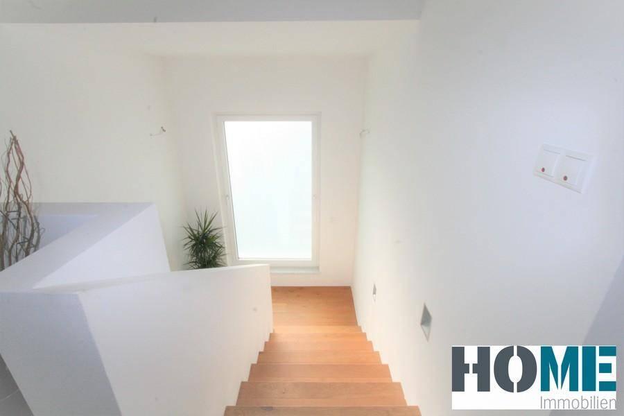 Treppenhaus mit Holzstufen und weißen Wänden, das viel Tageslicht durch ein Fenster erhält.